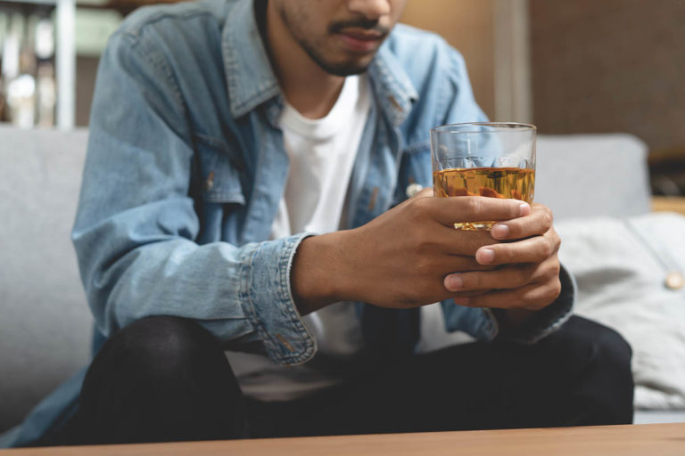 man distraught while holding alcoholic drink showing signs of alcohol abuse